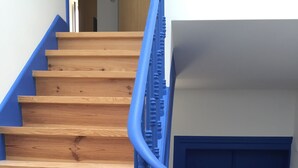 Eine hölzerne Treppe mit blauen Geländern und einer dunkelblauen Tür am Fuß.