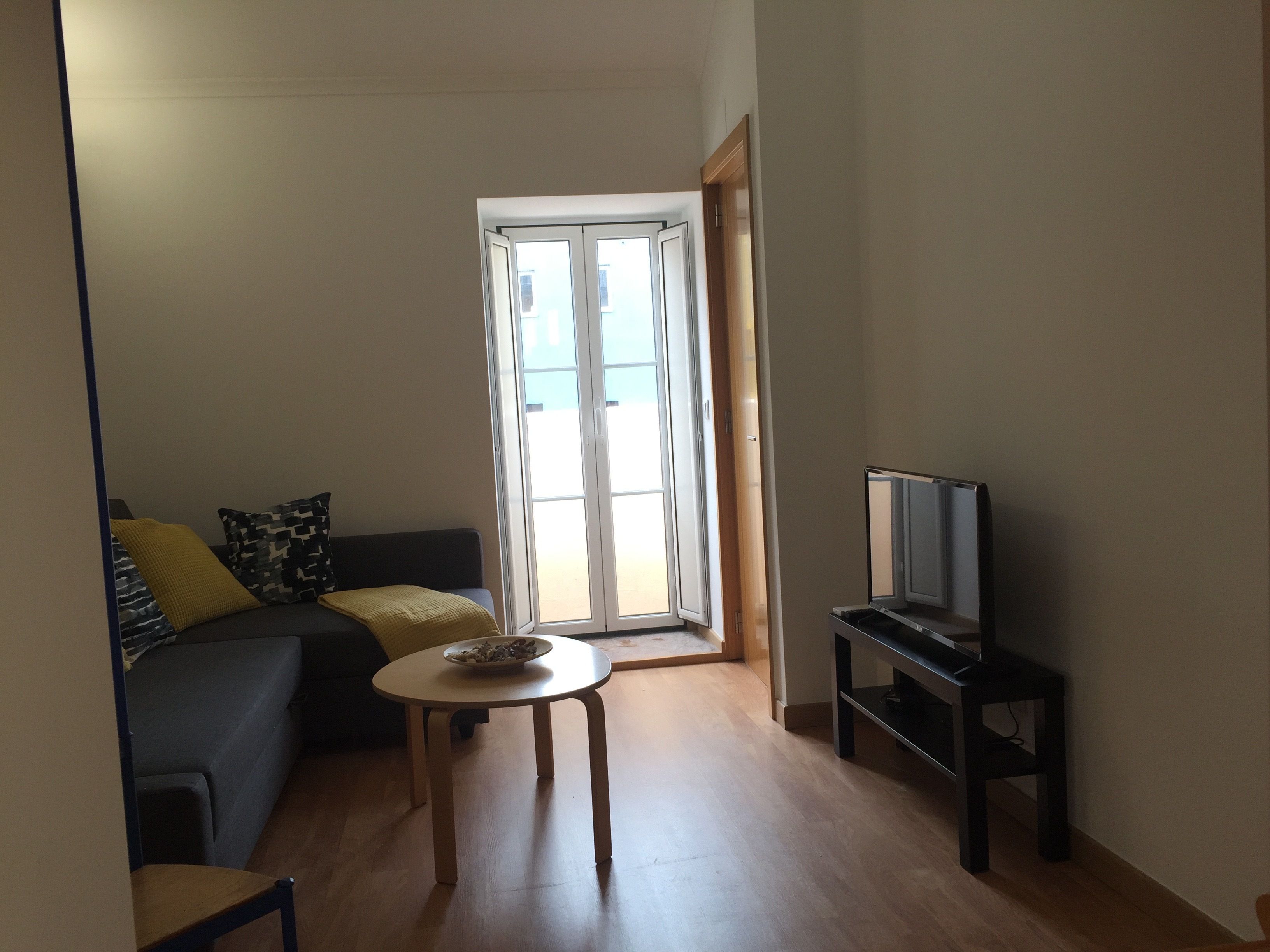 A living room with a sofa, a small round table, a television, and a sliding glass door leading to a balcony.