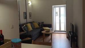 Ein Wohnzimmer mit einer Couch, einem Couchtisch, einem Fernseher und einer Tür, die auf einen Balkon führt.