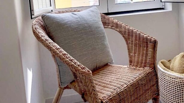 A wicker chair with a cushion in a room with a large window.