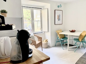 A modern kitchen with a kettle, a basket, and a dining area with teal chairs and a white table.