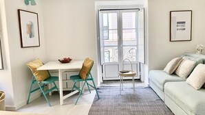 A compact living space with a dining area, a sofa, and a view through a glass door.