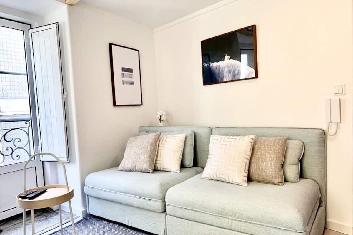 A room with two light green sofas, a small table with a remote control, a patterned rug, and two framed pictures on the wall.