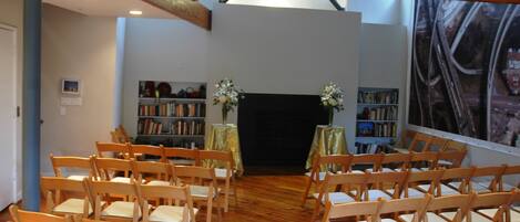 A room with wooden chairs arranged in rows, a fireplace, and bookshelves with books and decorative items.