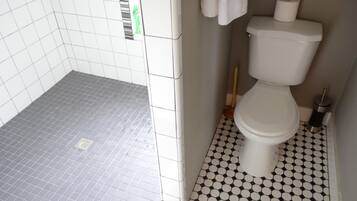 A bathroom with a shower area tiled in grey and a toilet area with black and white hexagonal tiles.