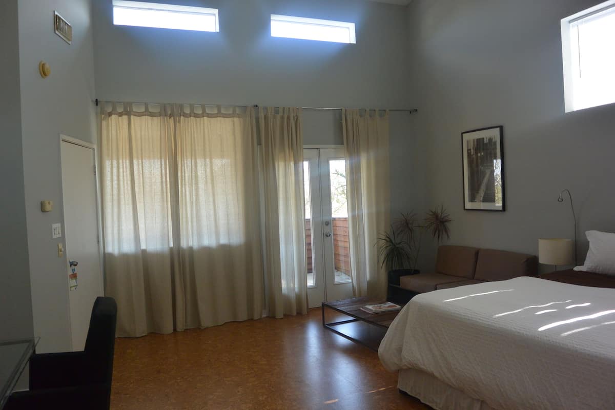 Un dormitorio con cama, sofá, mesa de centro, silla y puerta que da a un balcón.