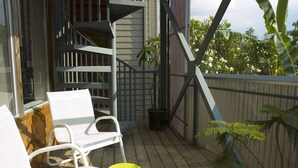 Een houten terras met witte stoelen en een gele kruk, een metalen trap en een bloempot.