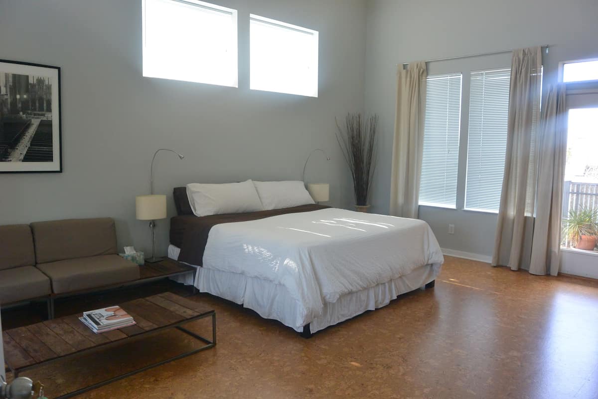 Un dormitorio con cama, sofá, mesa de centro y ventana con cortinas.