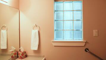 A bathroom with a window, a mirror, and a handrail.