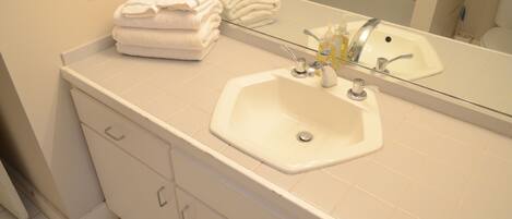 A bathroom with a white sink, a mirror, and a stack of white towels.