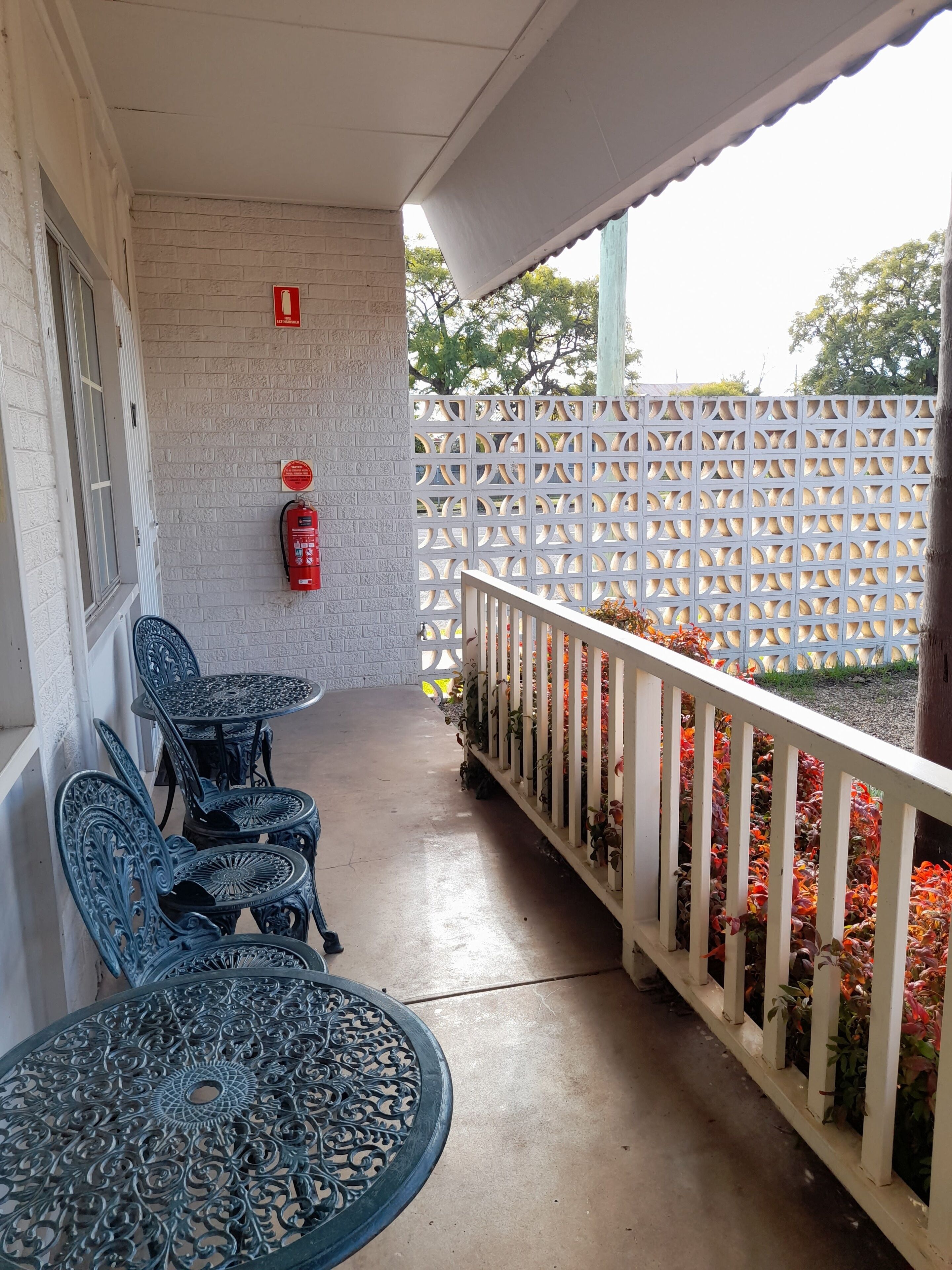 A covered outdoor area with a white fence, a fire extinguisher, and a table with chairs.