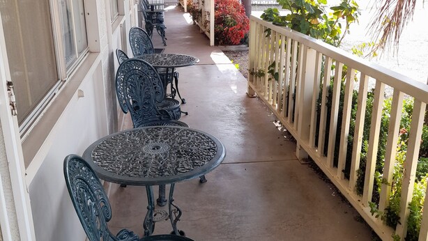 A covered outdoor seating area with metal tables and chairs, a white fence, and a view of the street. - Aromet Motor Inn (Temora)