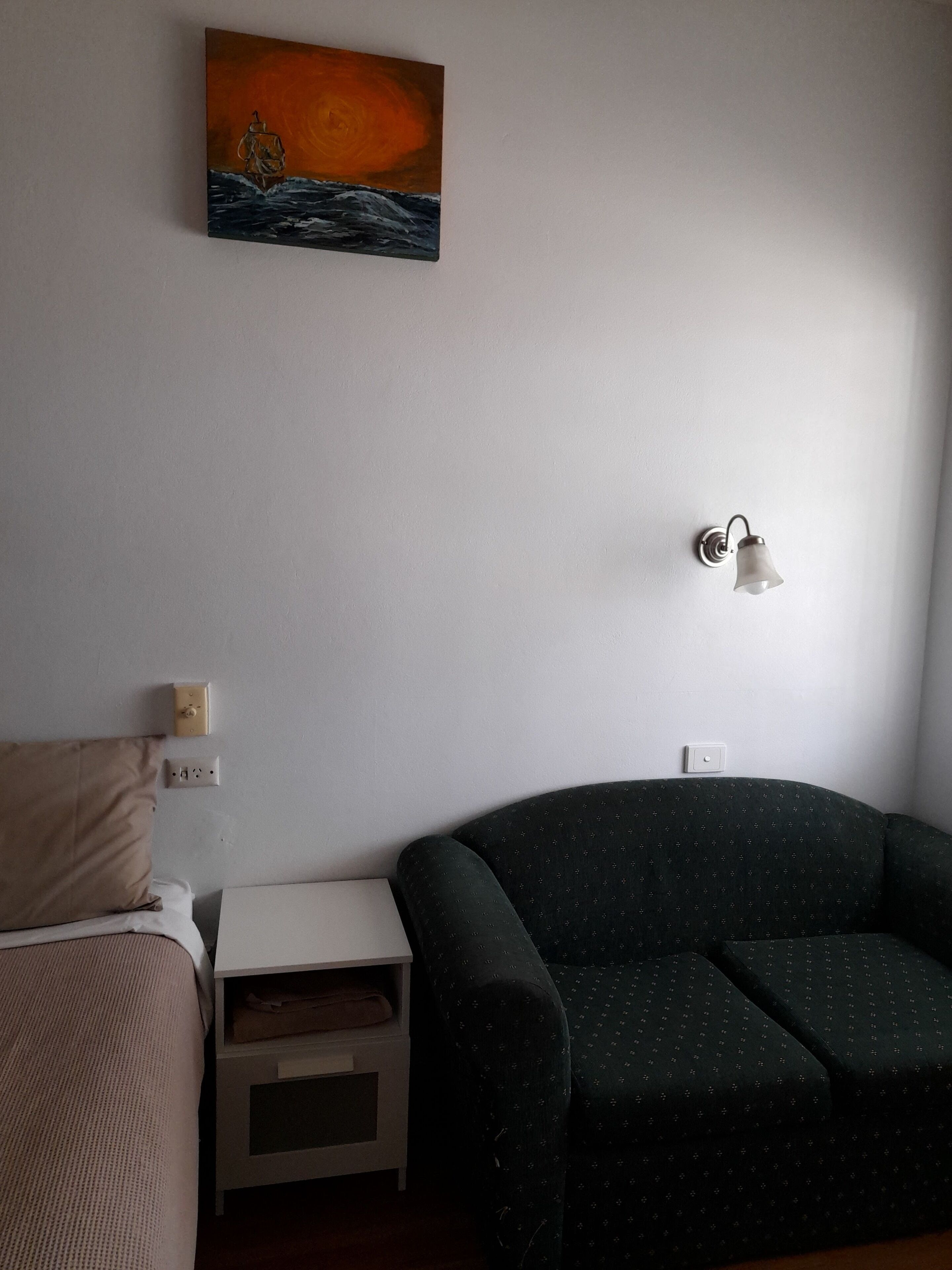 Una habitación con una cama, una mesita de noche, una lámpara y un sofá.