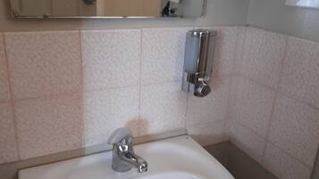 Un bany amb un lavabo blanc, un mirall i un dispensador de sabó sobre una estantàlia.