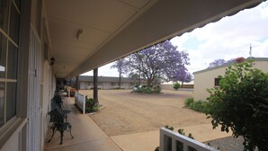A covered outdoor area with a gravel path, a tree with purple flowers, and a building with a white facade.