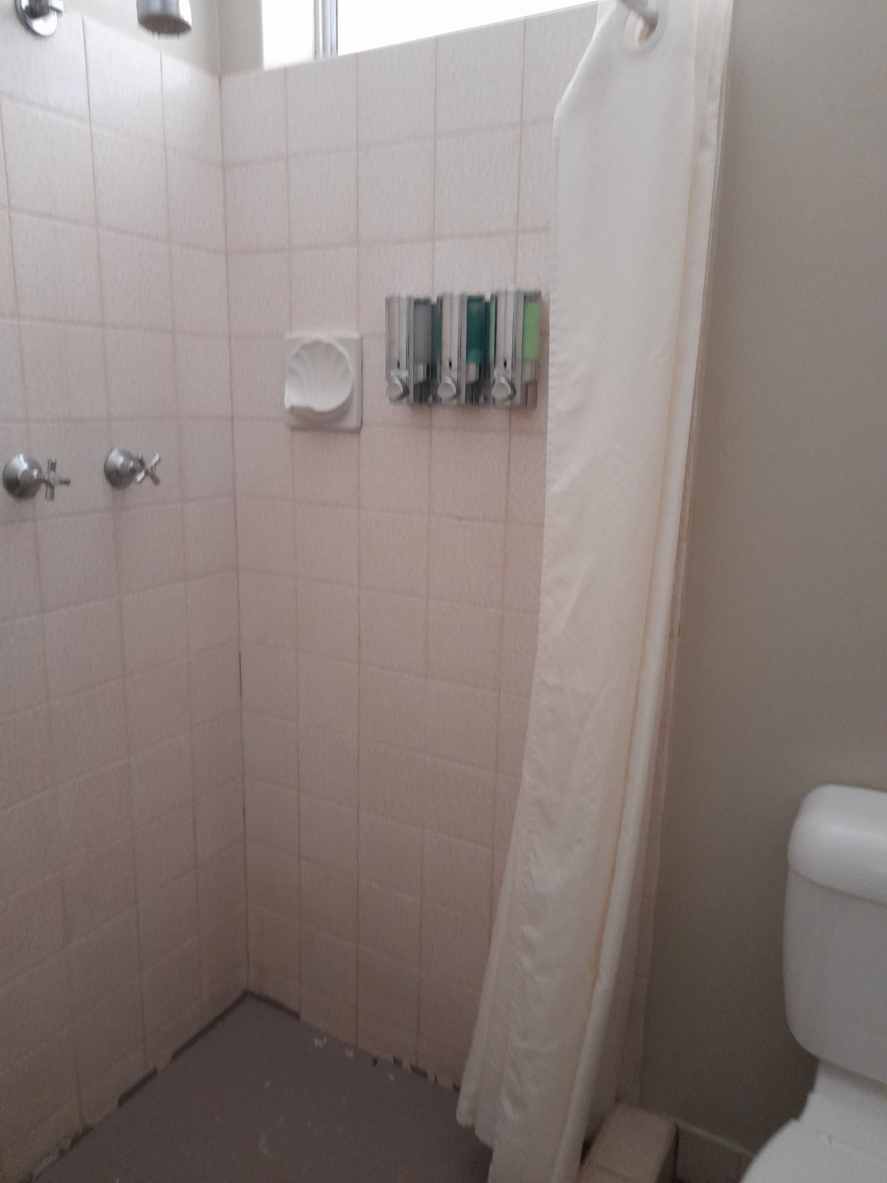 A bathroom with white tiles, a shower curtain, a toilet, and a soap dispenser mounted on the wall.