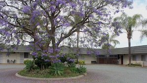 A building with a reception area, a covered outdoor seating area, and a gravel driveway. - Aromet Motor Inn (Temora)