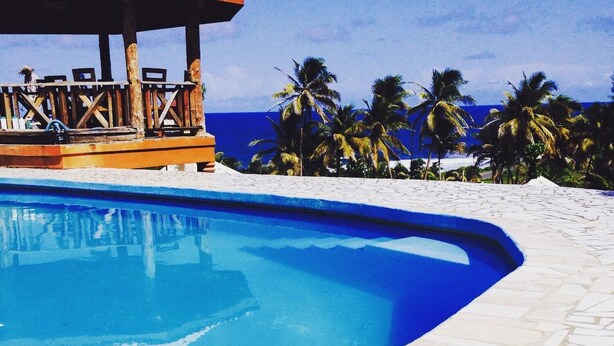 A swimming pool with a curved edge, surrounded by a tiled deck. - Spring Gardens Resort (Biabou)