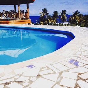 A swimming pool with a curved edge, surrounded by a tiled deck. - Spring Gardens Resort (Biabou)