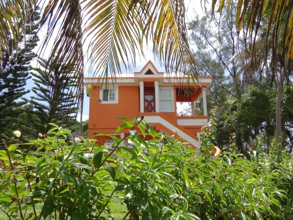 A two-story building with a white and orange exterior, surrounded by lush greenery and palm trees. - Spring Gardens Resort (Biabou)