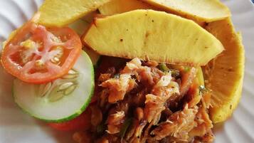 Um prato com carne desfiada, fatias de fruta amarela, uma fatia de tomate e uma fatia de pepino.