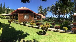 A wooden building with a red roof, surrounded by a well-maintained garden with various shrubs and palm trees. - Spring Gardens Resort (Biabou)