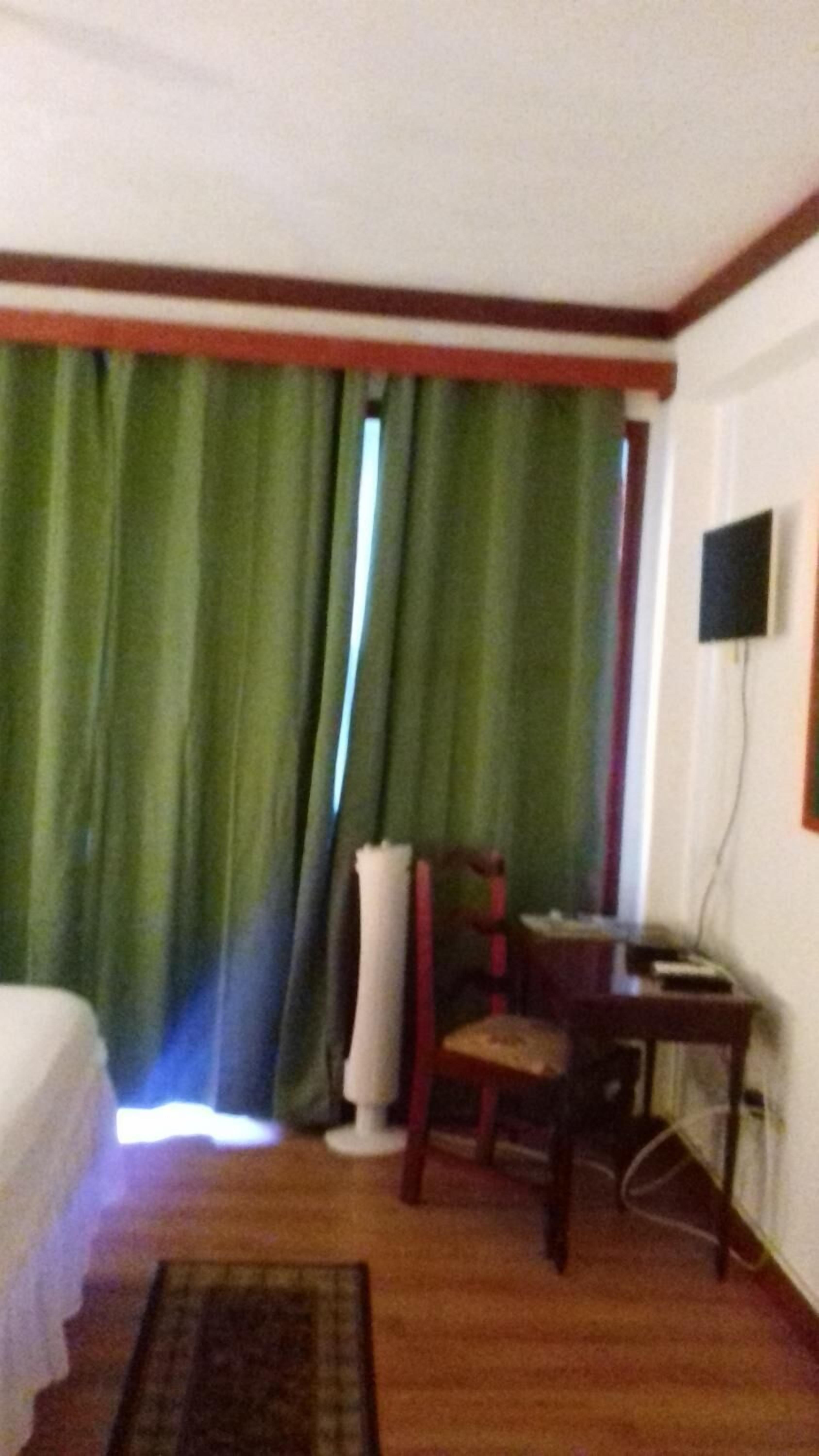 Quarto de hotel com cama, poltrona, escrivaninha e televisão.