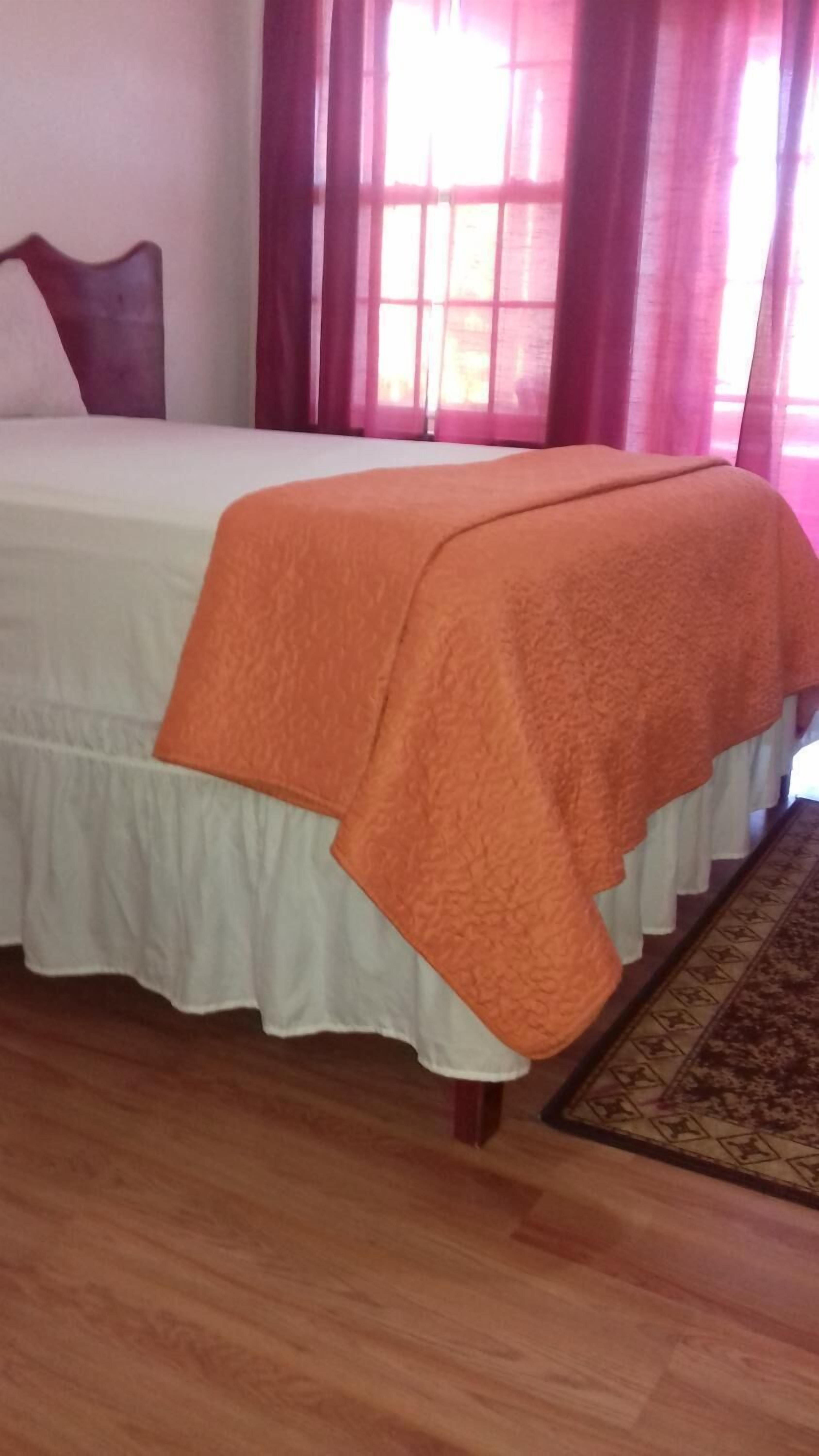 A bed with an orange blanket, a white bed skirt, and a wooden floor.