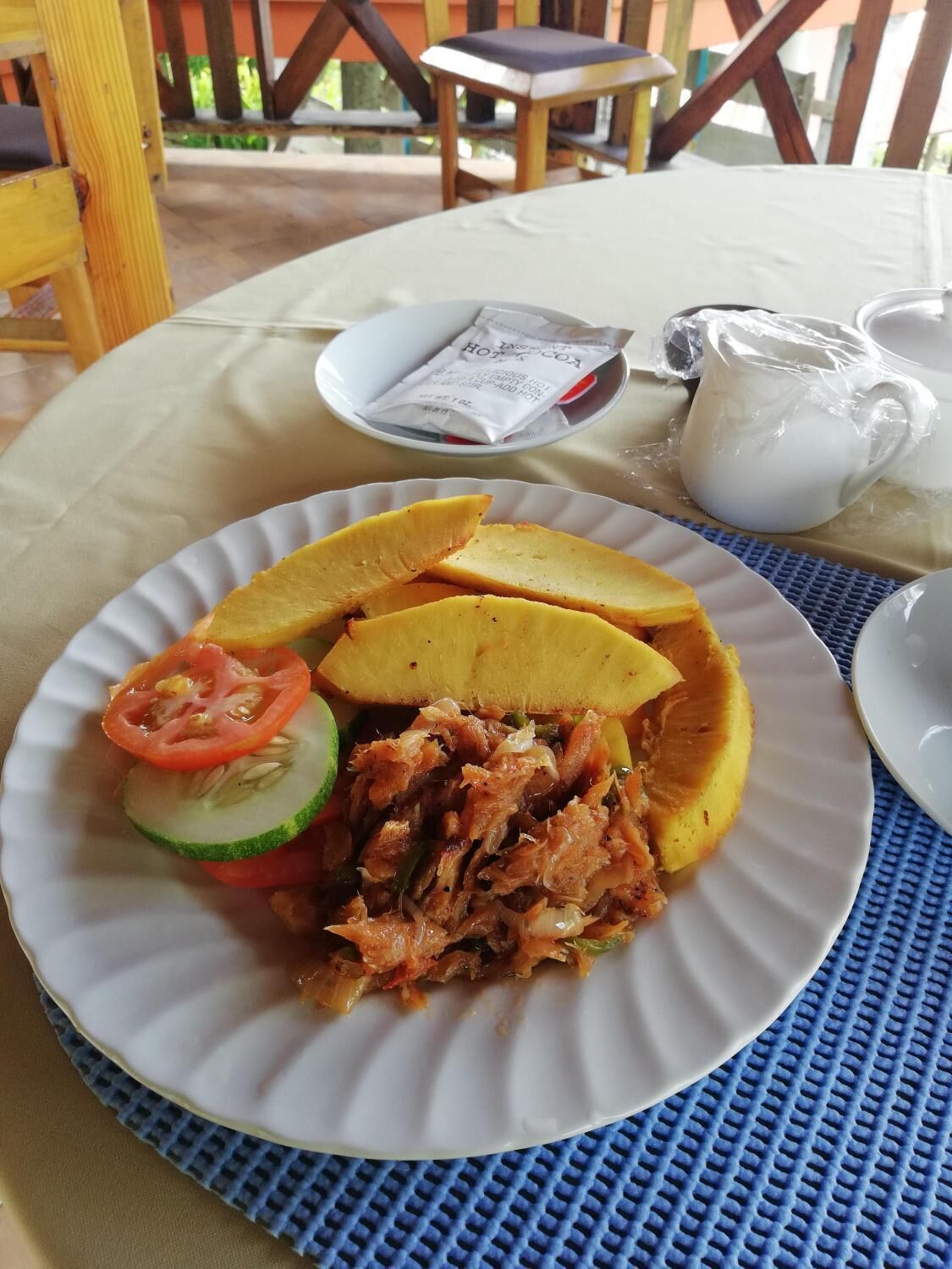 A plate of food with sliced plantains, shredded meat, and a slice of tomato and cucumber.
