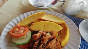 A plate of food with sliced plantains, shredded meat, and a slice of tomato and cucumber.