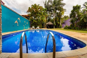 Una piscina con agua azul cristalina, rodeada de palmeras y un muro turquesa.