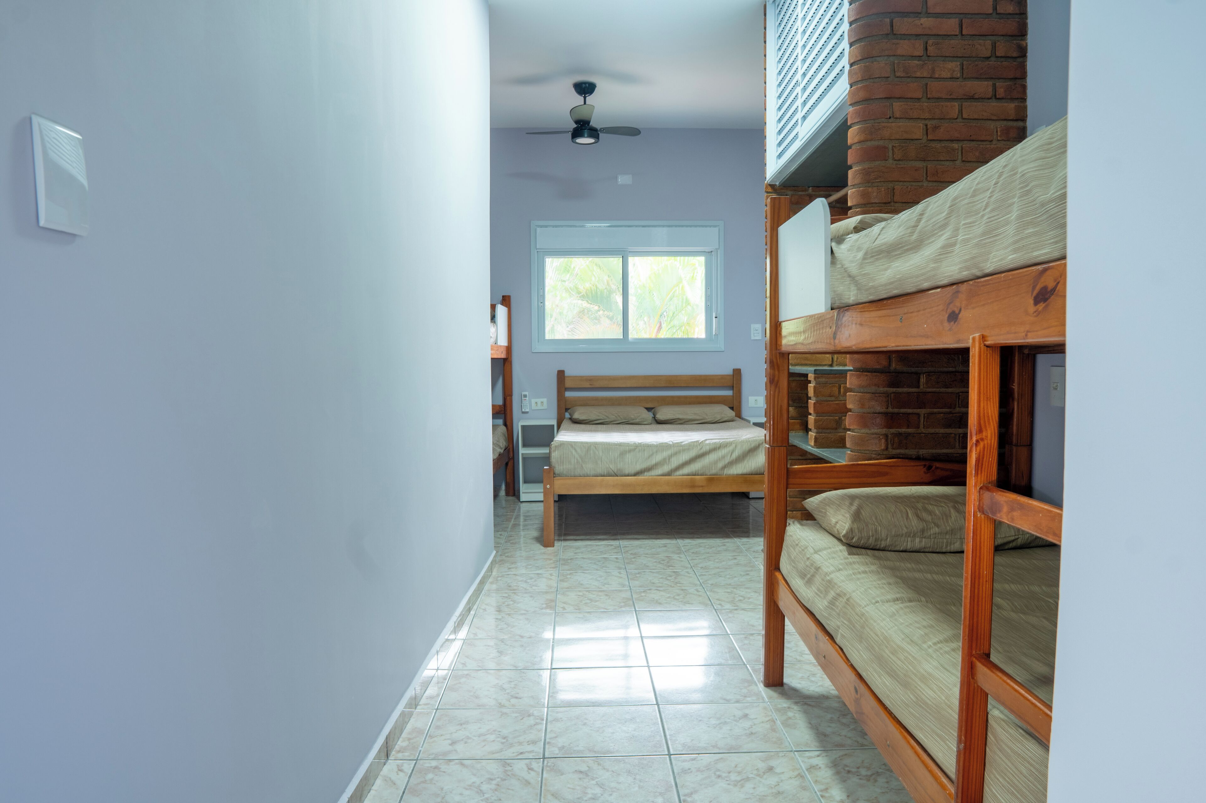 A room with bunk beds, a ceiling fan, a window, and a tiled floor.