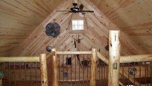 Una habitación de madera con techos altos, techo inclinado, ventilador de techo, ventana y una rústica verja de madera.