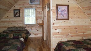 Un dormitorio de cabaña acogedor con dos camas, paredes de madera, una ventana y obras de arte enmarcadas.