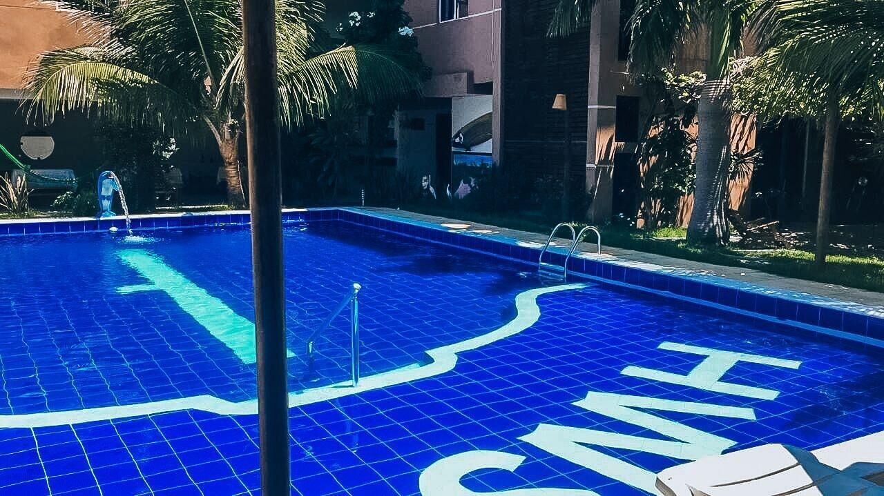 Una piscina con suelo de azulejos azules y un gran logotipo en forma de 'H'.