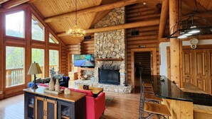 L’intérieur d’une cabane en rondins, avec une cheminée en pierre, des meubles en bois et de grandes fenêtres.