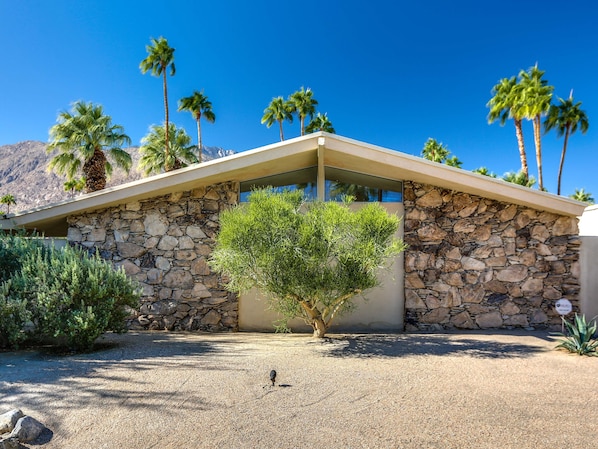 A modern house with a stone facade, palm trees, and a gravel driveway.