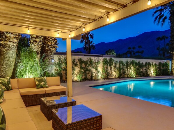 An outdoor pool area with a covered seating area, a pool, and a view of mountains.