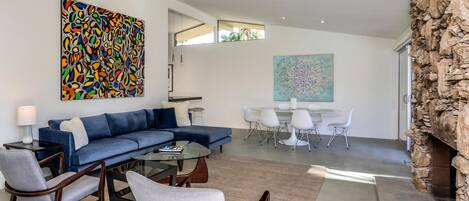 A modern living room with a sectional sofa, a glass coffee table, and a dining area with a round table and chairs.