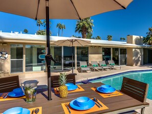 A poolside dining area with a table set for two, a pineapple, and a pitcher of water.
