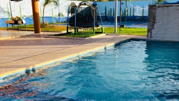 Ein Swimmingpool mit Rutsche, umgeben von einer Betonplattform und Palmen.
