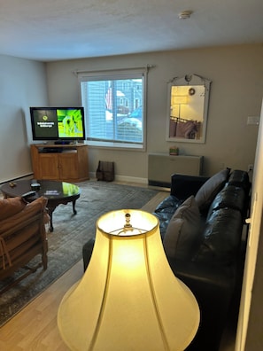 Sala de estar com televisão, sofá, luminária e janela com persianas.