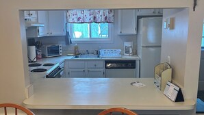 Eine Küche mit weißen Schränken, einem eingebauten Backofen, einem Kühlschrank und einem Fenster mit Blumenverhang.