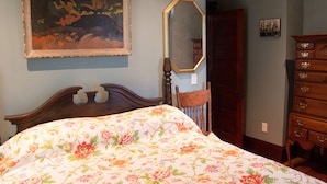 Quarto com colcha florida, cabeceira de madeira, um espelho grande e um penteado com várias gavetas.
