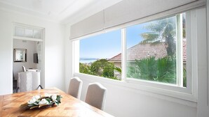 A dining area with a wooden table and chairs, a large window with a view of a coastal area, and a white interior.