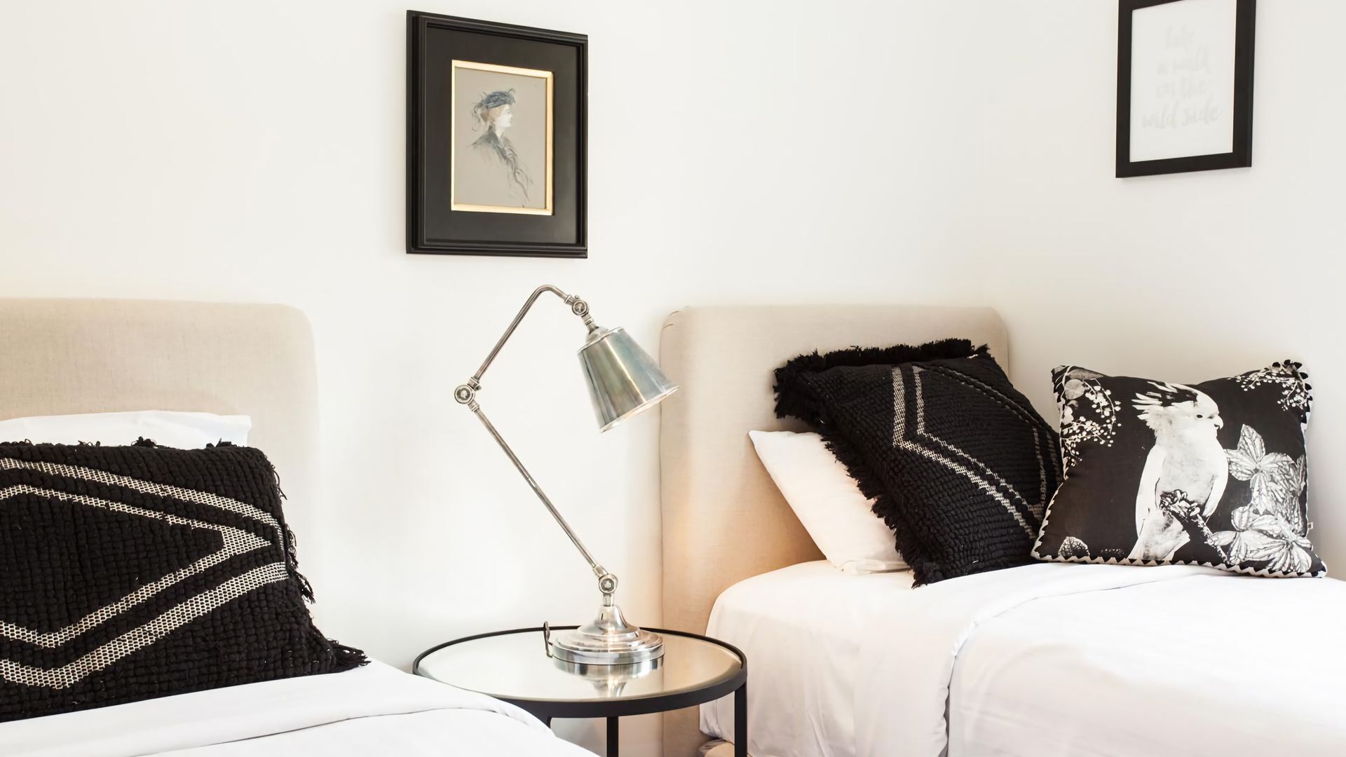 A bedroom with a bed, a side table with a lamp, and two framed pictures on the wall.