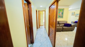 A hallway with wooden doors, a tiled floor, and a brown leather sofa with purple cushions in the background.