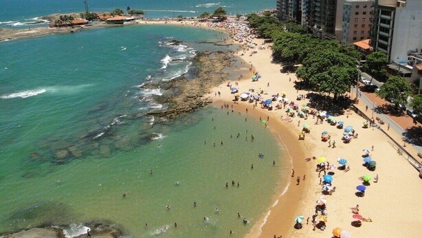 A beach with clear waters, a sandy shore, and buildings in the background.