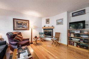 A living room with a fireplace, a television, and a bookshelf. - Near Mtn/Steps to Free Bus-Pool-Hot Tub-Patio-W/D (Steamboat Springs)