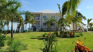 A multi-story hotel with a flat roof, surrounded by palm trees and a well-maintained lawn. - Condo w/Views, Beach, Htd Pool, Pickleball, Golf Cart,Gym, Walk to Restaurant (Governors Harbour)